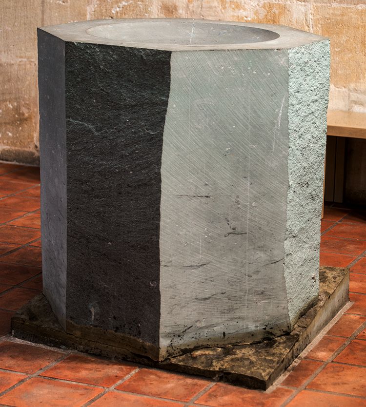 der Taufstein mit seinen gespaltenen und gesägten Seiten auf dem Posament in unterschiedlicher Steinformation.